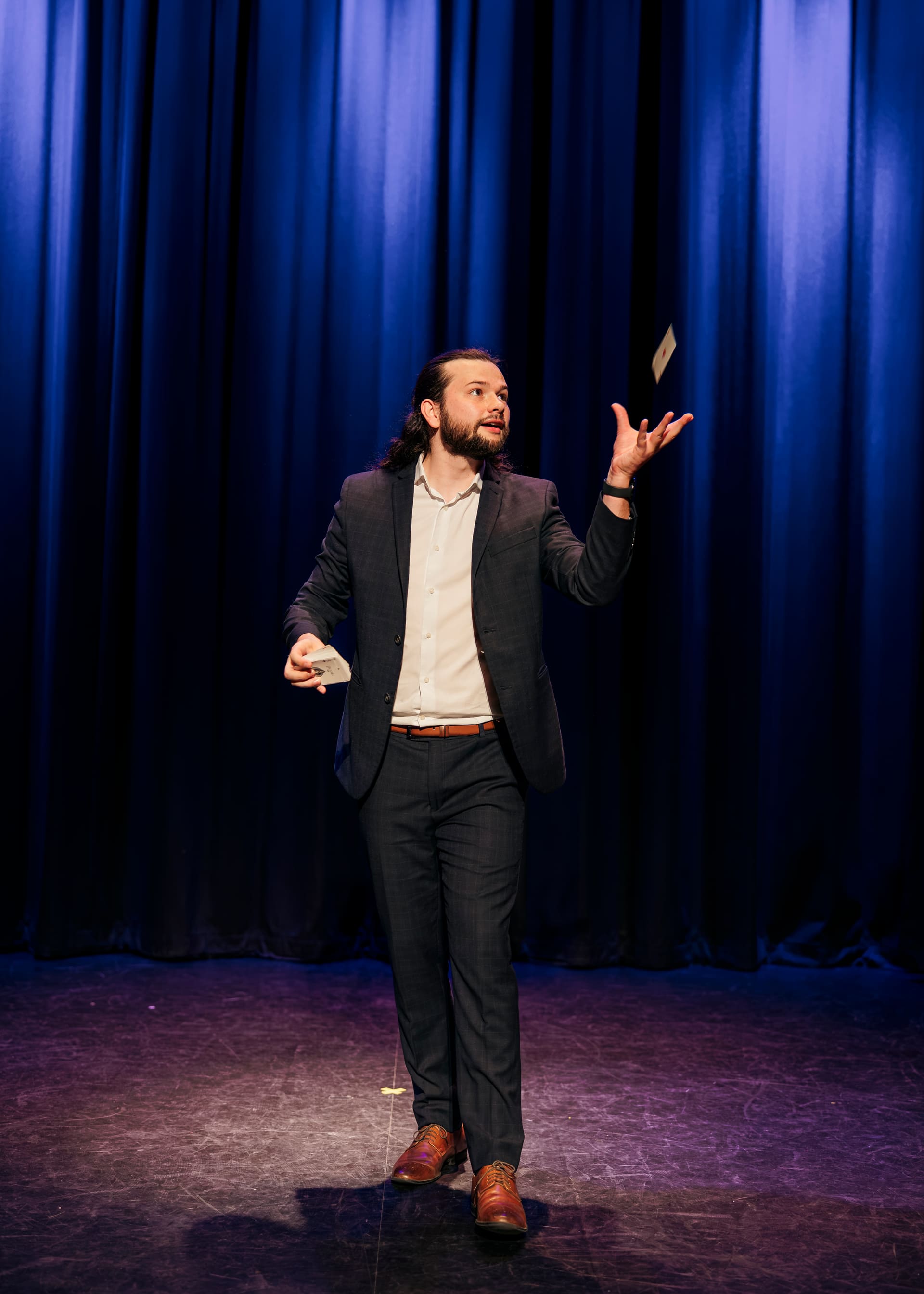 Magician Callum McClure catching a playing card in mid-air on stage