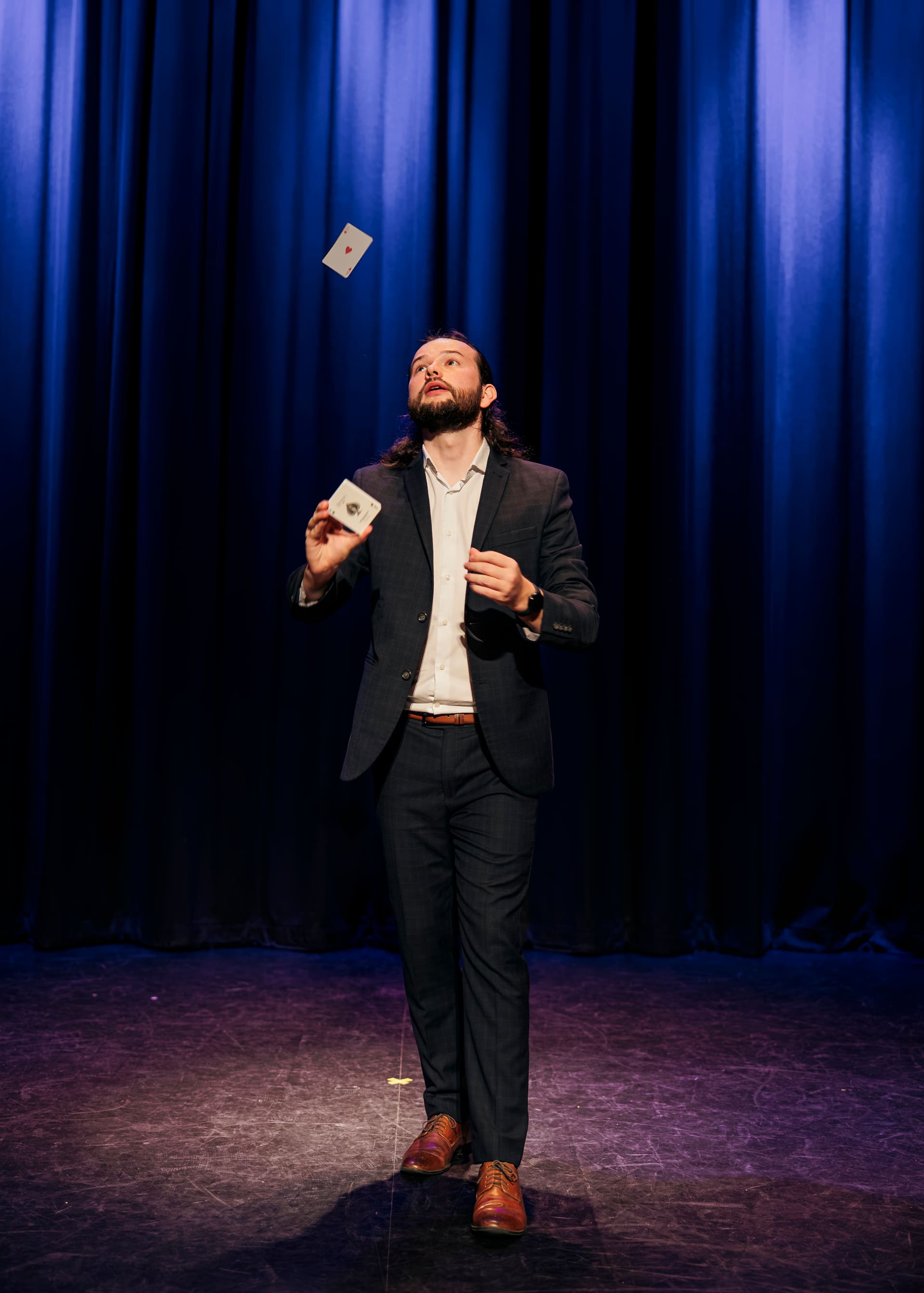 Magician Callum McClure tossing the ace of hearts into the air on stage